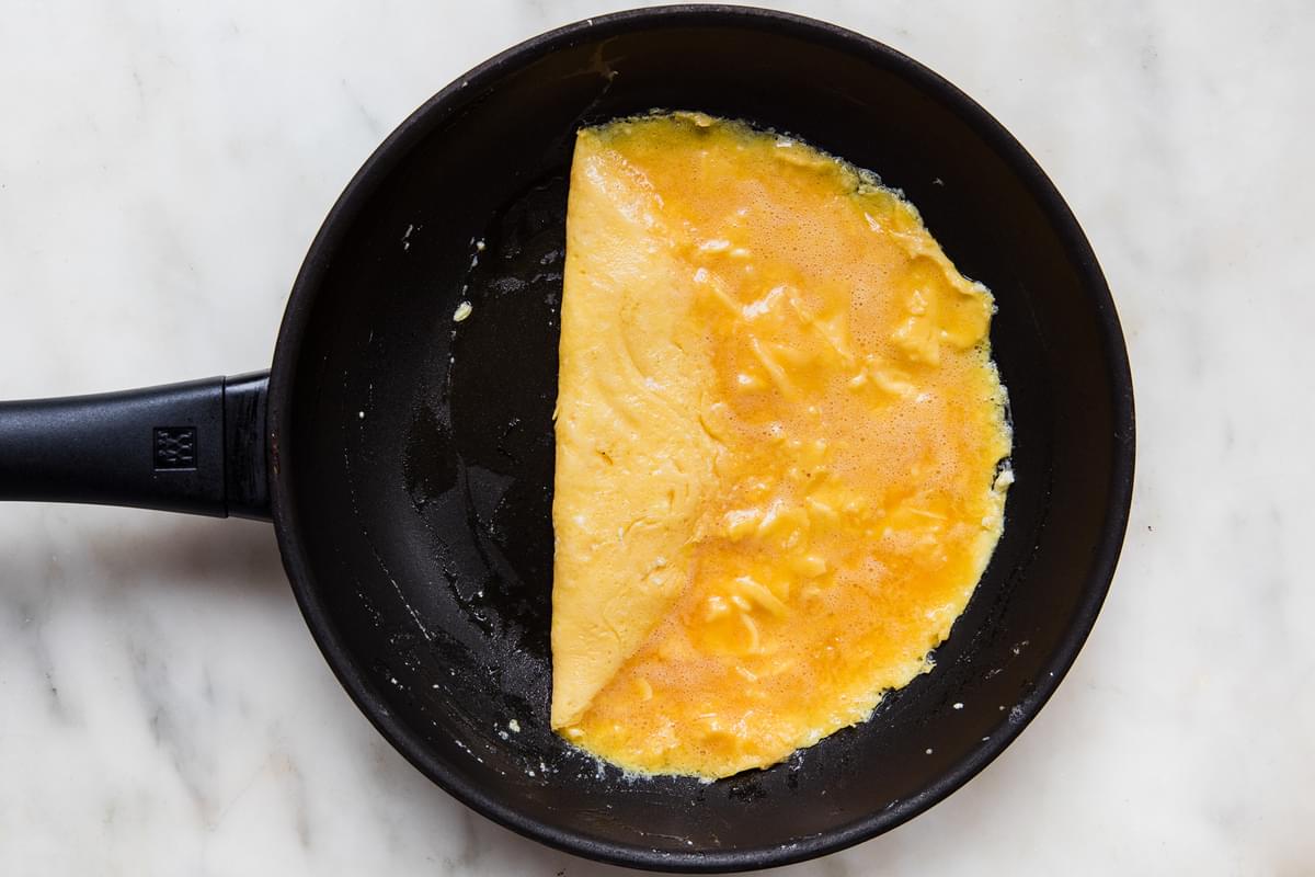 a homemade French omelette being rolled in a non stick frying pan with pan with melted butter