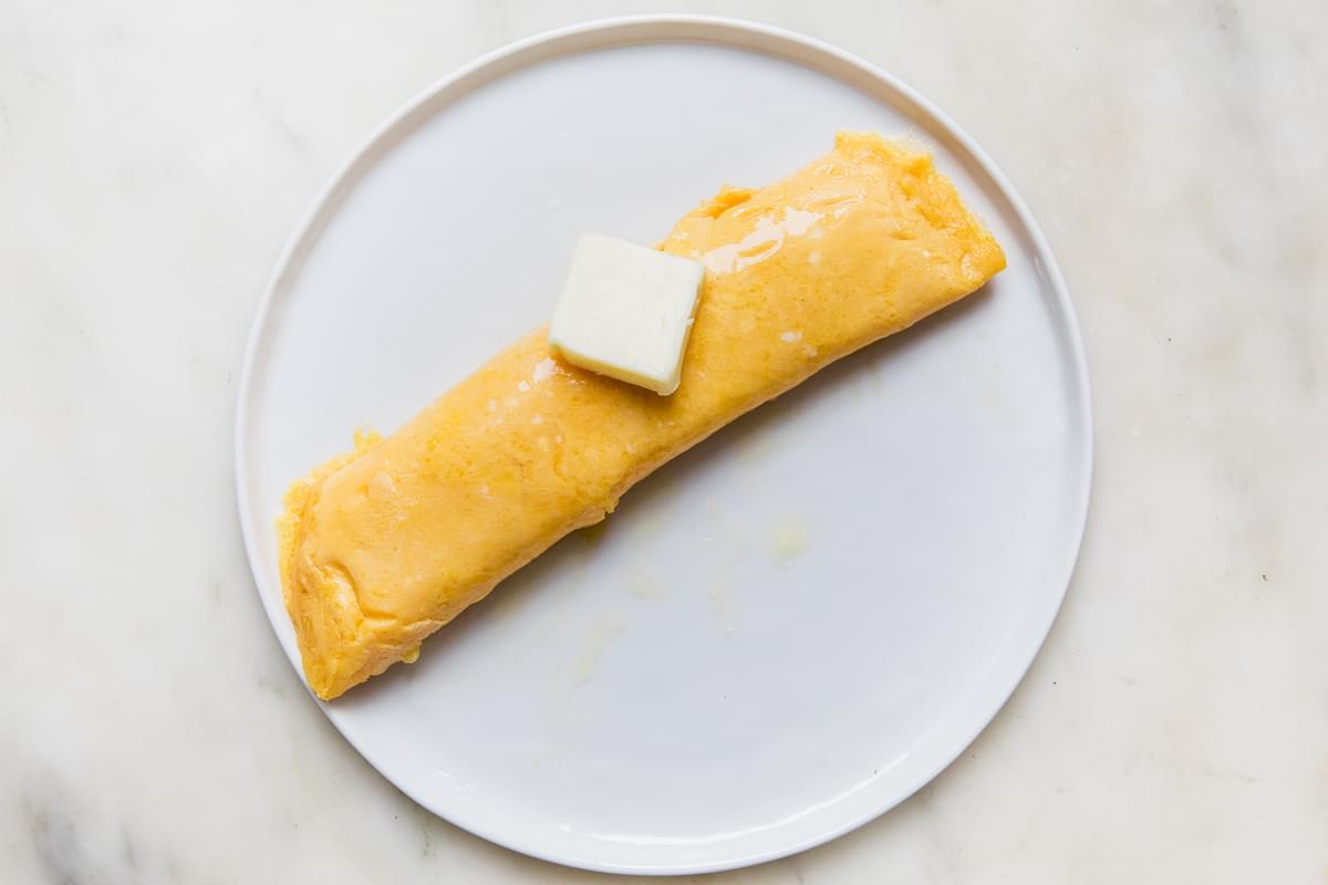 a homemade French omelette on a plate topped with a slice of butter