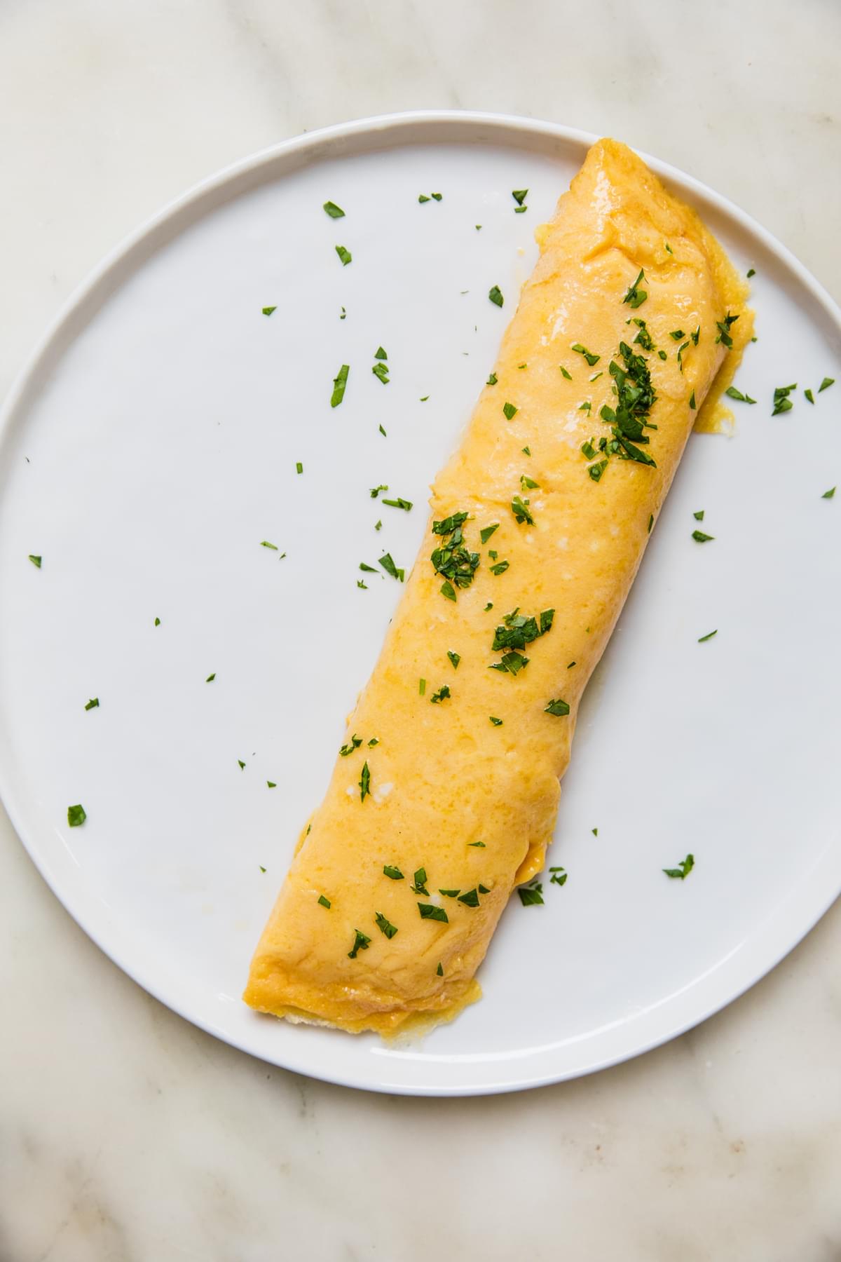 a homemade French omelette on a plate topped with butter and chopped parsley