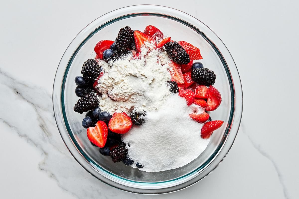 fresh blackberries, blueberries, raspberries and sliced strawberries in a glass bowl sprinkled with flour, sugar and salt