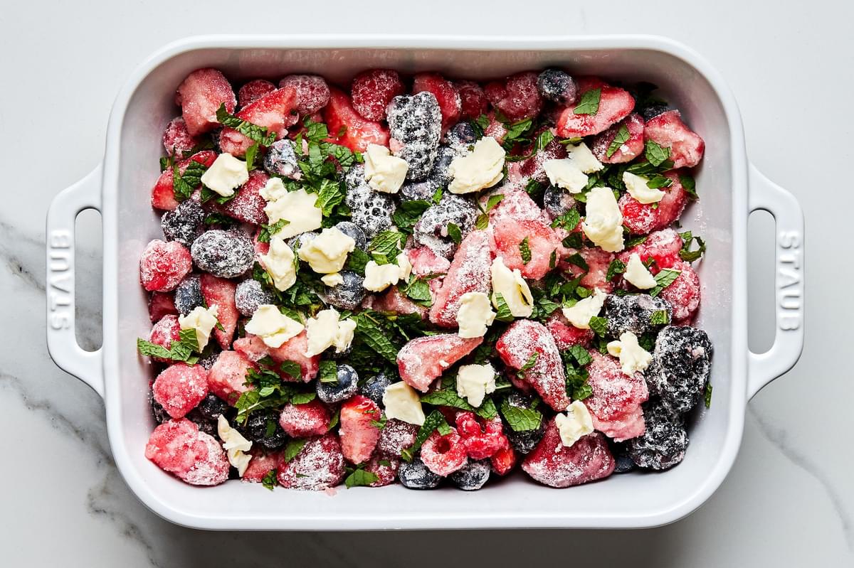 fresh berries mixed with with flour, sugar and salt in a 9x13 pan topped with pads of butter and fresh mint leaves