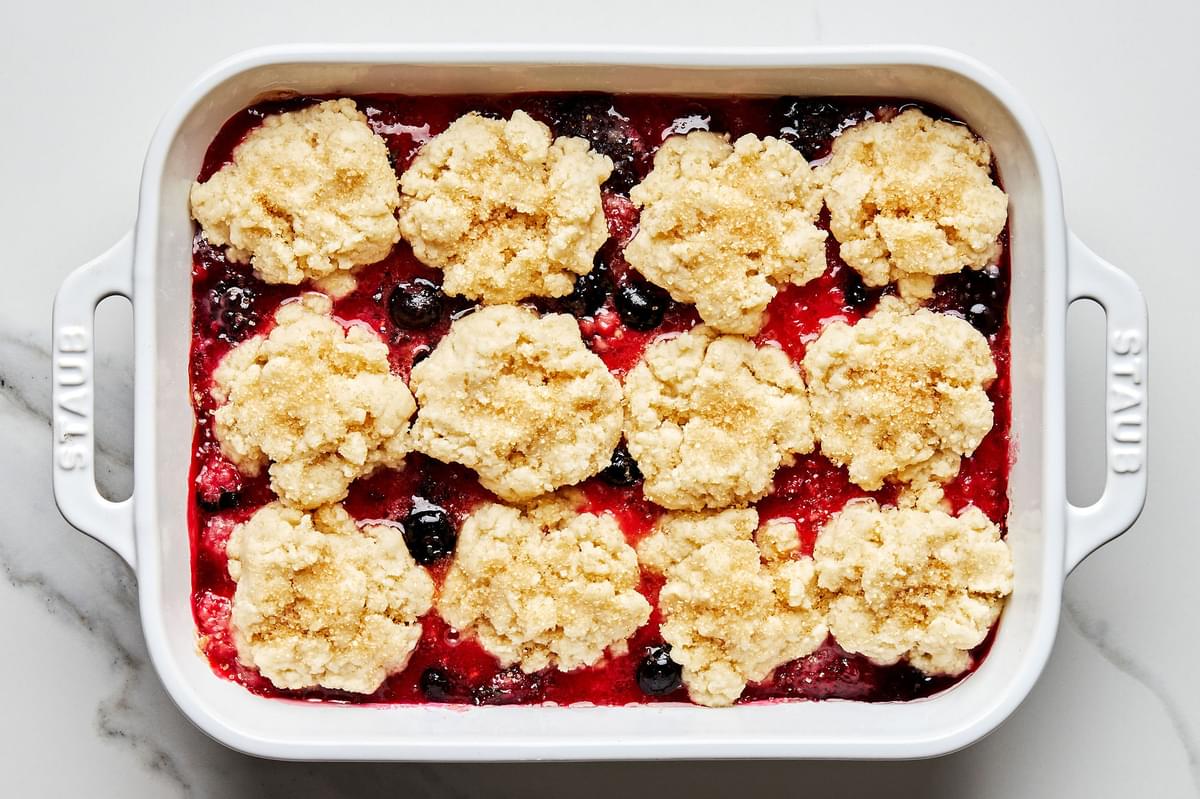 mixed fresh berries and mint leaves that have been baked in the oven topped with cobbler dough biscuits