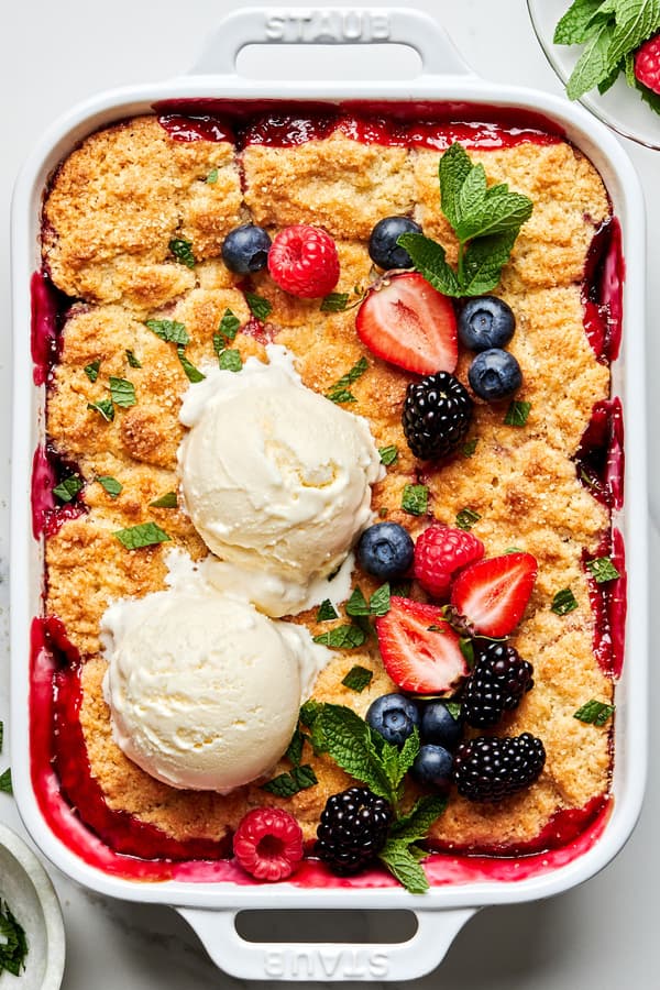 fresh berry cobbler in a 9x13 baking dish topped with 2 scoops of vanilla ice cream, additional fresh berries and fresh mint