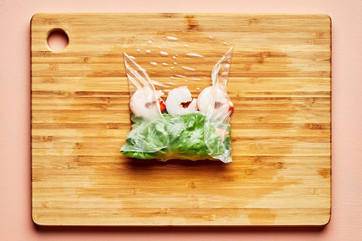 rice paper topped with lettuce, vermicelli rice noodles, julienned vegetables and shrimp being rolled on a cutting board