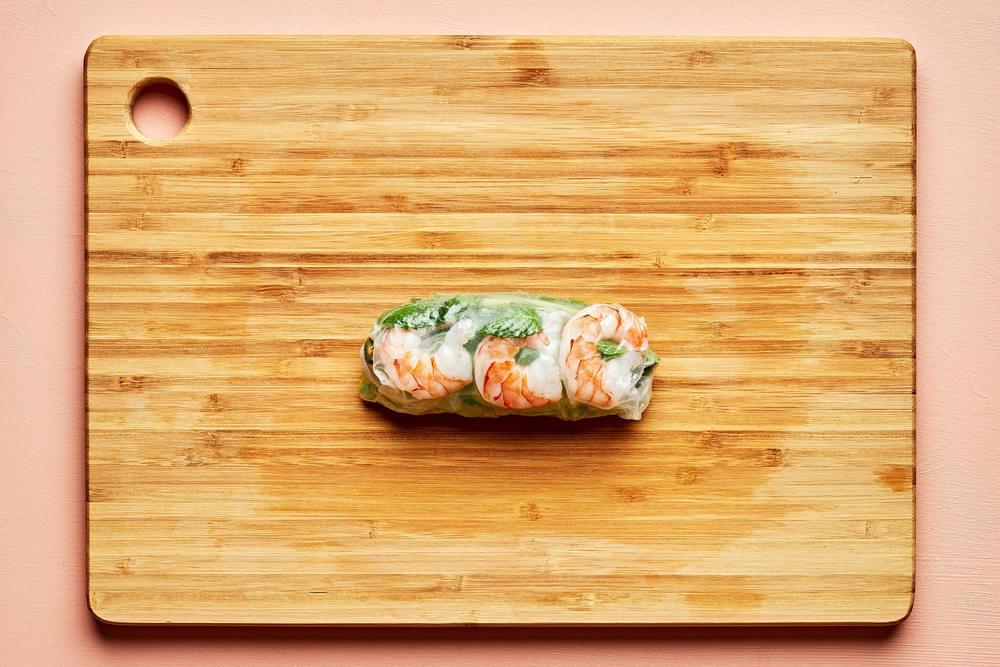 a fresh spring roll on a cutting board filled with lettuce, vermicelli rice noodles, julienned vegetables and shrimp