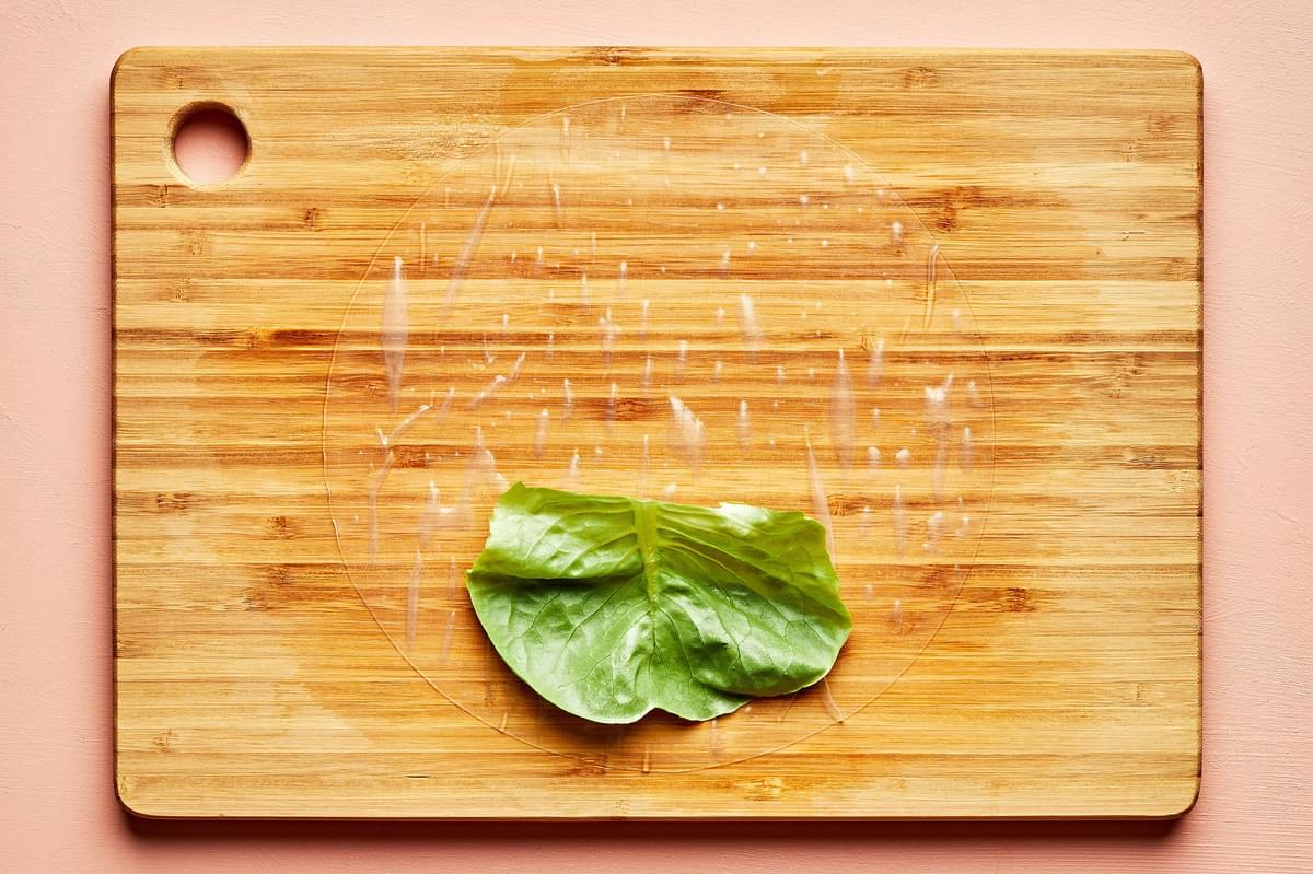 rice paper with a piece of lettuce on top on a wooden cutting board