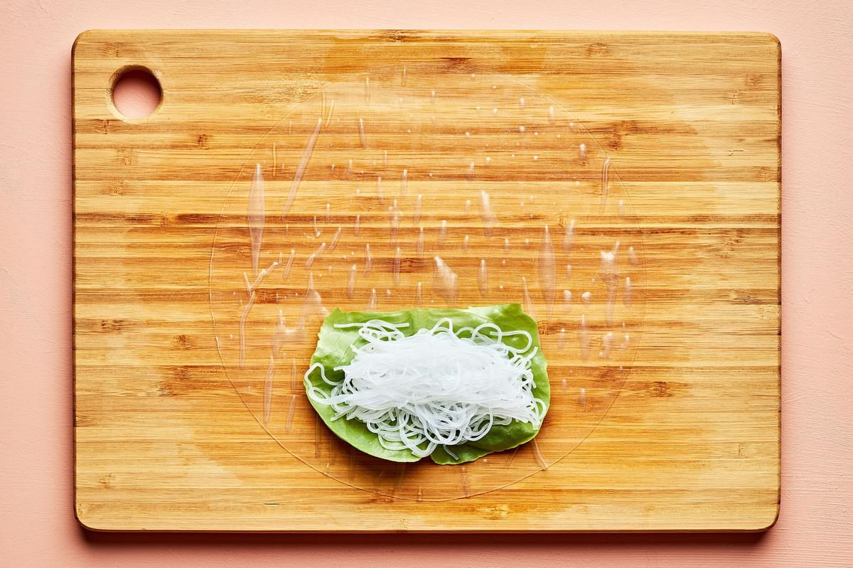 rice paper topped with lettuce and vermicelli rice noodles on a wooden cutting board
