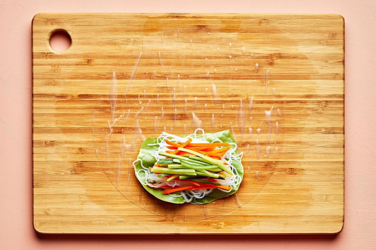 rice paper topped with lettuce, vermicelli rice noodles and julienned vegetables on a wooden cutting board