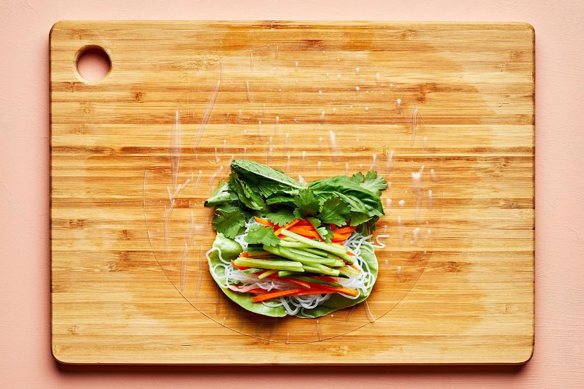 rice paper topped with lettuce, vermicelli rice noodles, julienned vegetables and fresh herbs on a wooden cutting board