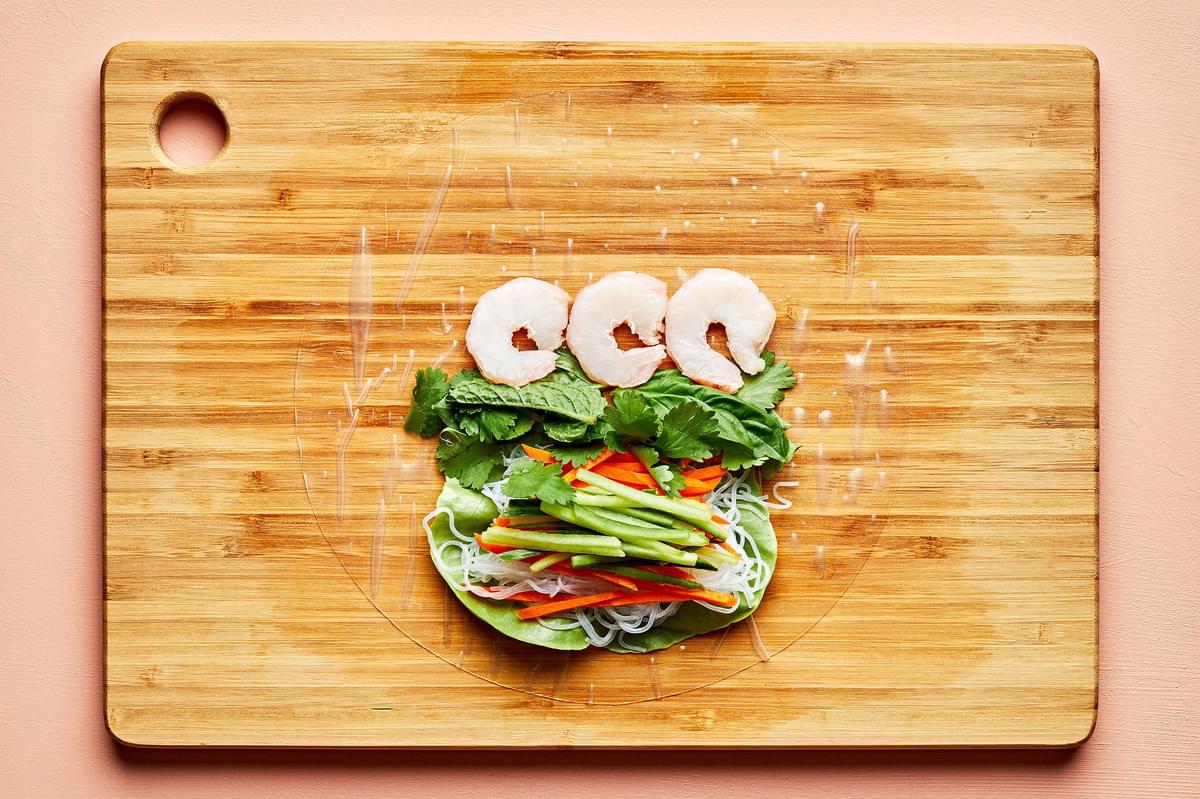 rice paper topped with lettuce, vermicelli rice noodles, julienned vegetables and shrimp on a cutting board