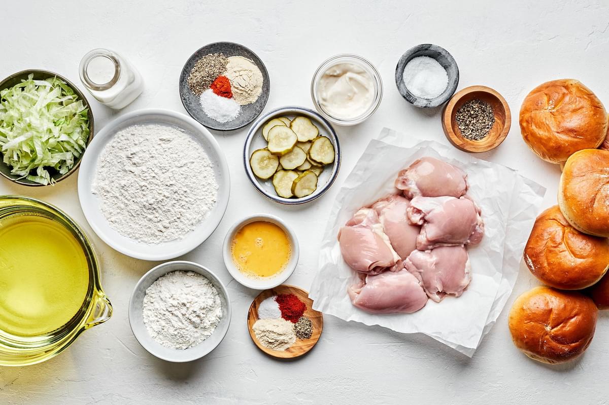 ingredients to make homemade fried chicken sandwiches in bowls including pickles, garlic aioli, lettuce and brioche buns