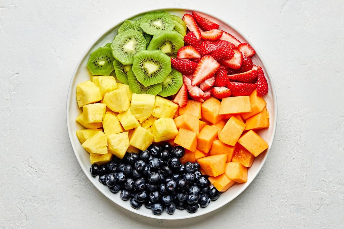 chopped Cantaloupe, Pineapple , Strawberries, Blueberries and Kiwis in sections on a platter for making fruit salad