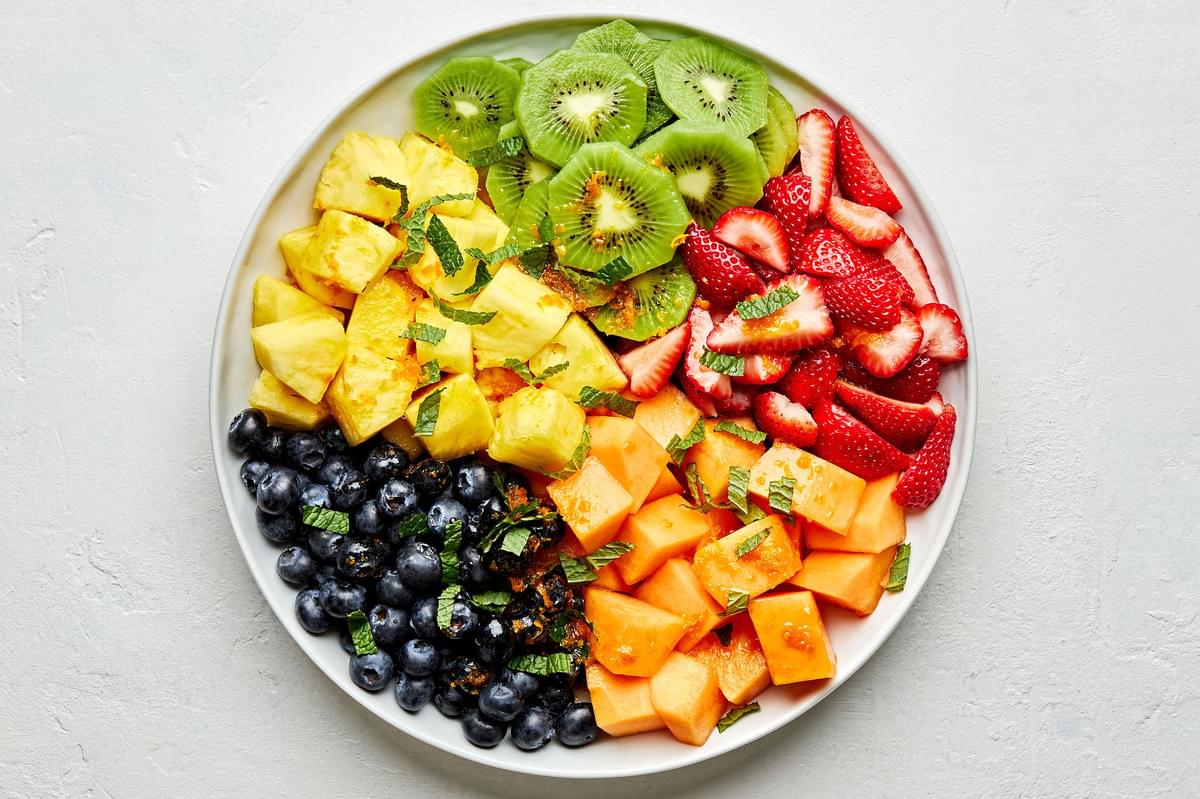 chopped Cantaloupe, Pineapple , Strawberries, Blueberries and Kiwis in on a platter topped with mint and orange dressing