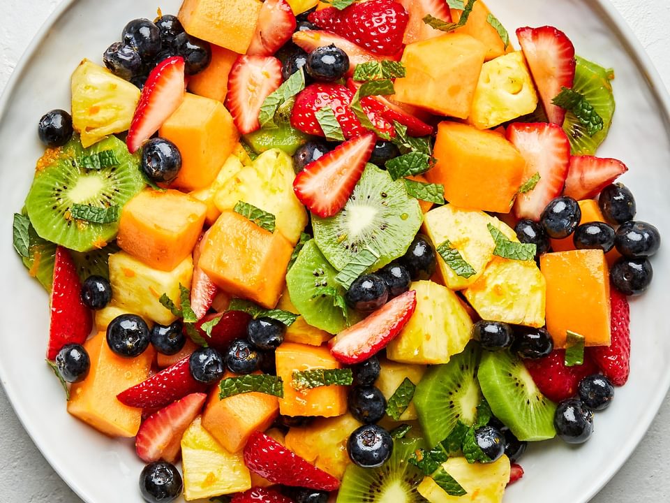 homemade fruit salad mixed with an orange juice dressing and mint leaves on a platter on the counter