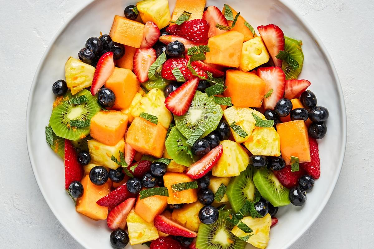 fruit salad Cantaloupe, Pineapple , Strawberries, Blueberries and Kiwis mixed with mint and orange dressing on a platter