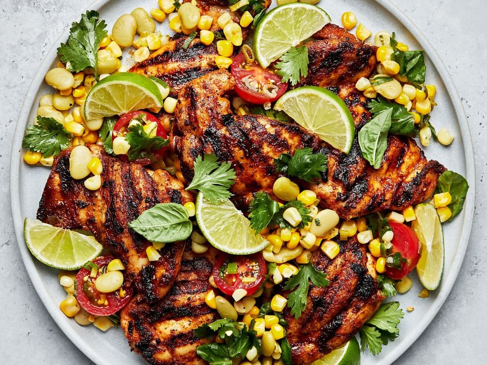 Grilled chicken Thighs with Succotash on a serving platter topped with lime wedges for garnish