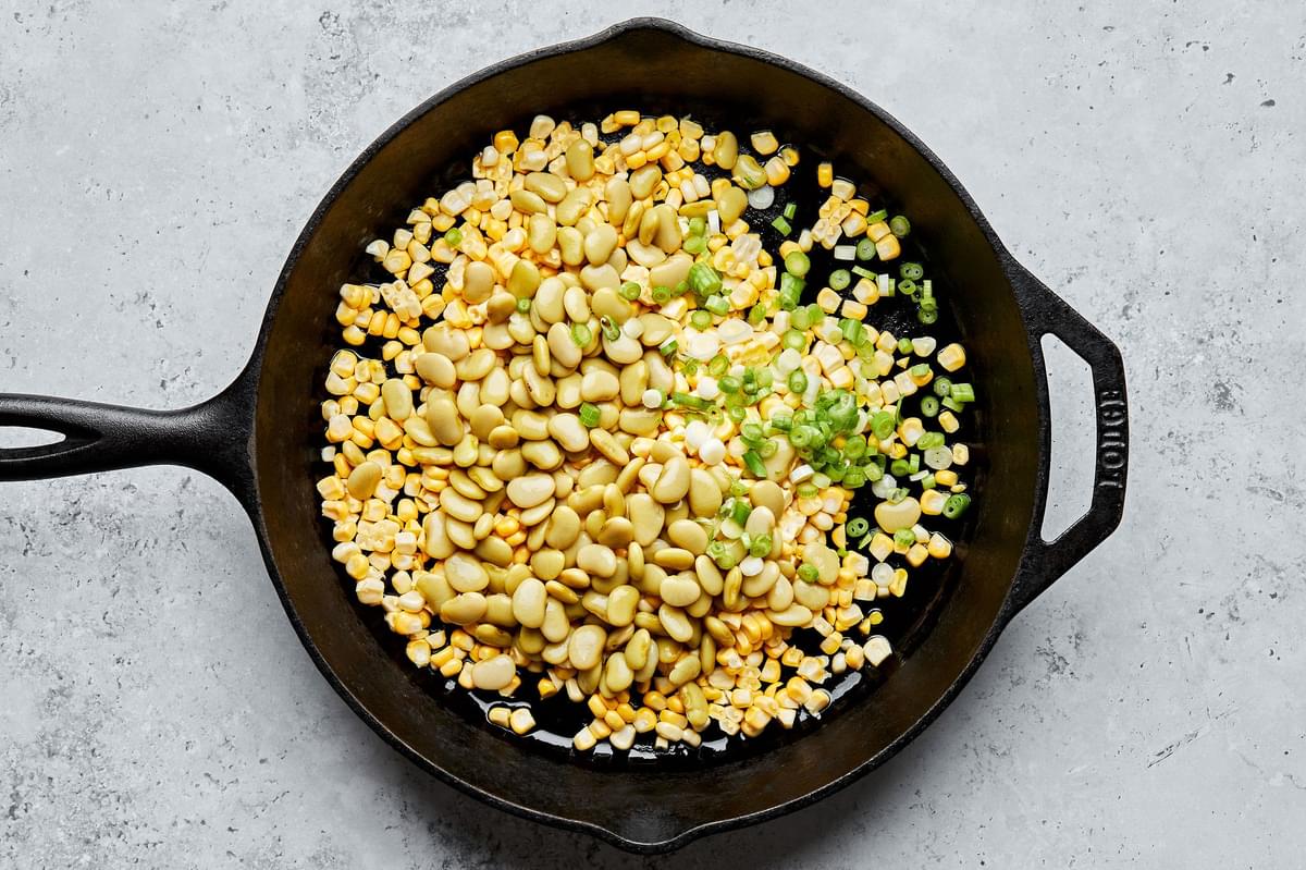 lima beans, corn and green onions being cooked in a skillet with olive oil