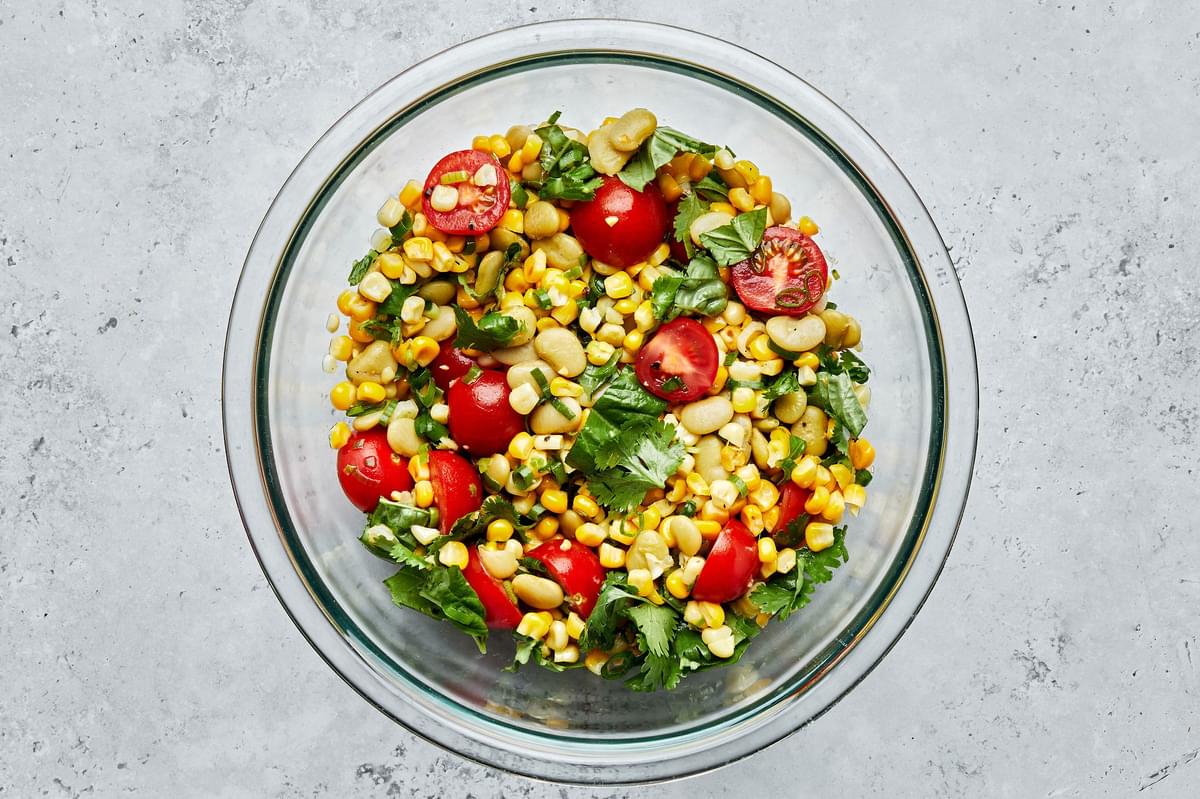 Homemade succotash in a glass bowl made with lima beans, corn, green onion, tomato, cilantro basil, lime juice, salt & pepper
