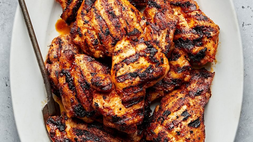 Grilled chicken thighs with beautiful grilled marks on a platter with a serving fork