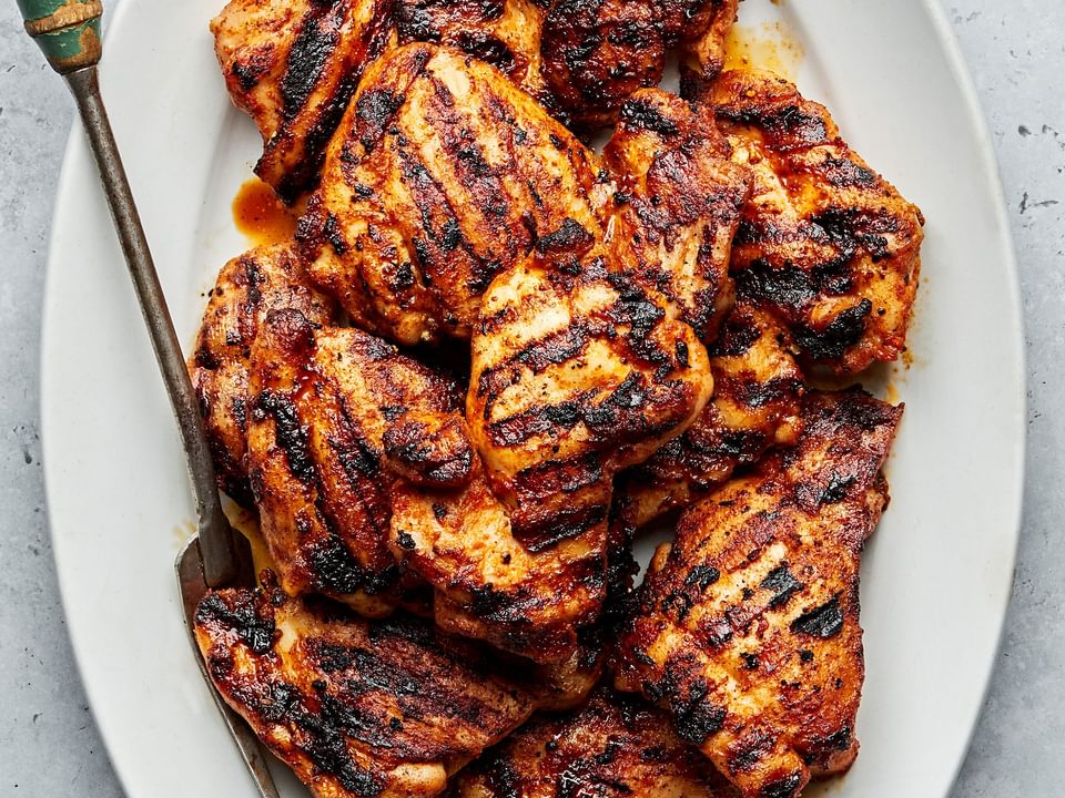 Grilled chicken thighs with beautiful grilled marks on a platter with a serving fork