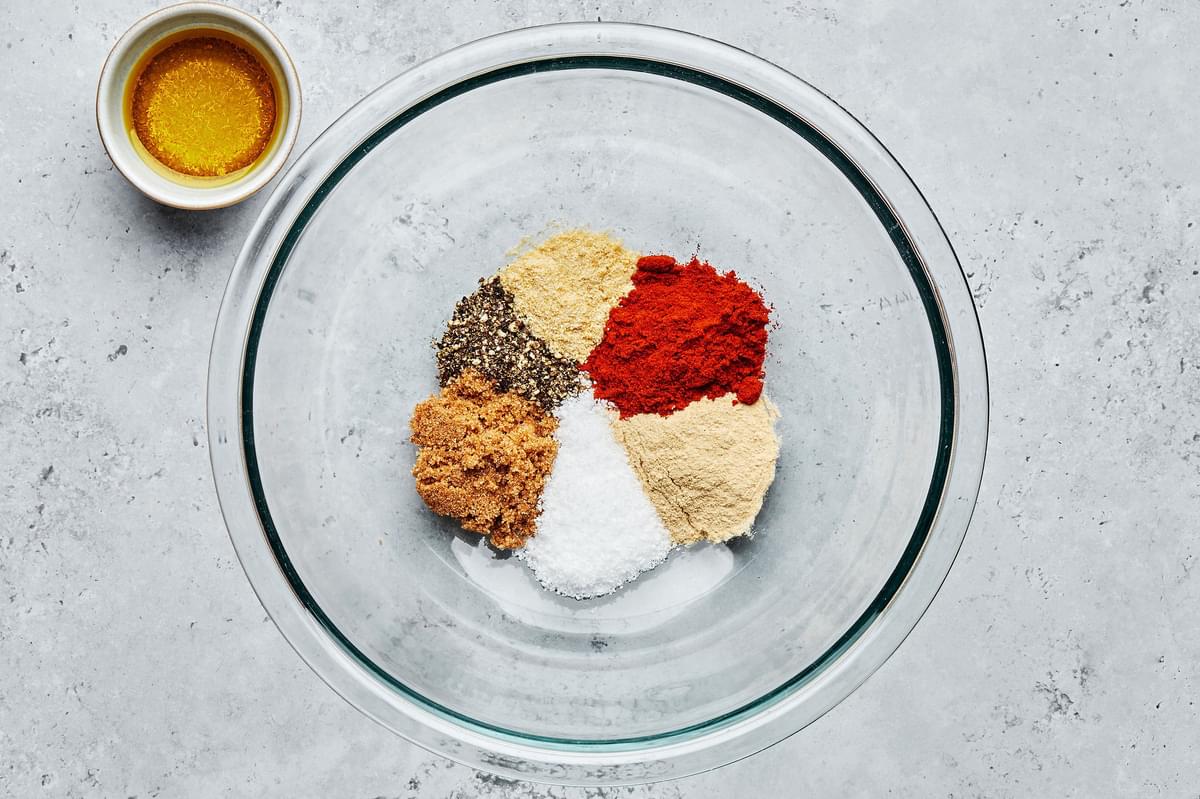 brown sugar, salt, garlic powder, onion powder, paprika & pepper in a glass bowl beside a small bowl of olive oil