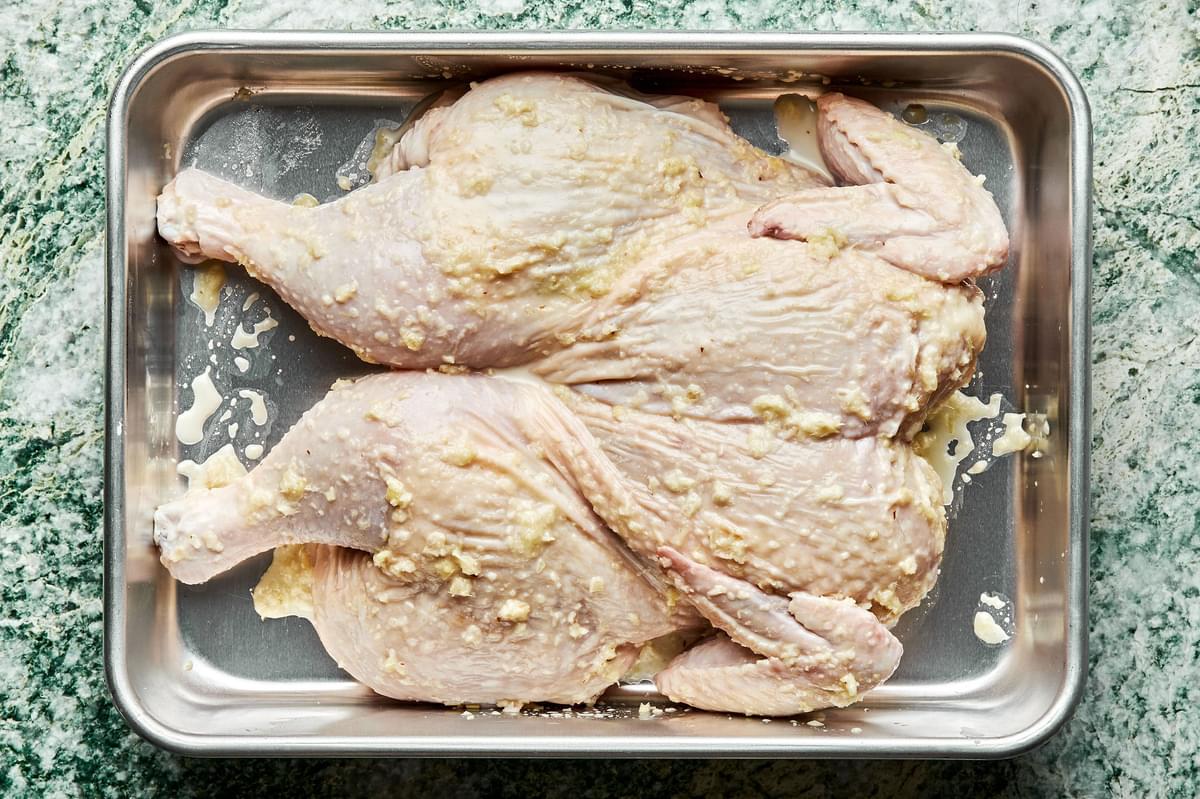 a spatchcocked chicken on a baking sheet covered with lemongrass paste made of ginger, garlic, lemongrass, honey, oil & salt