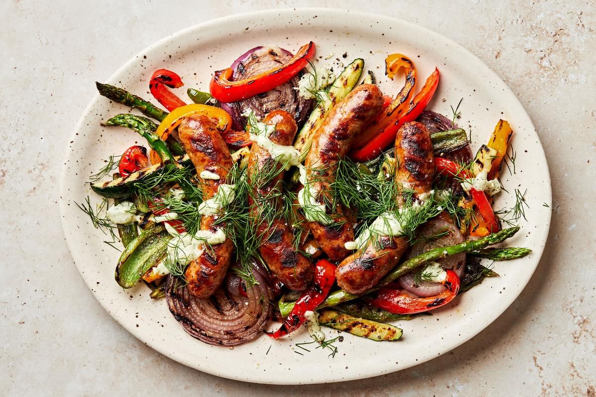 Grilled sausages and vegetables dried with creamy dill dip and sprinkled with fresh dill on a serving platter