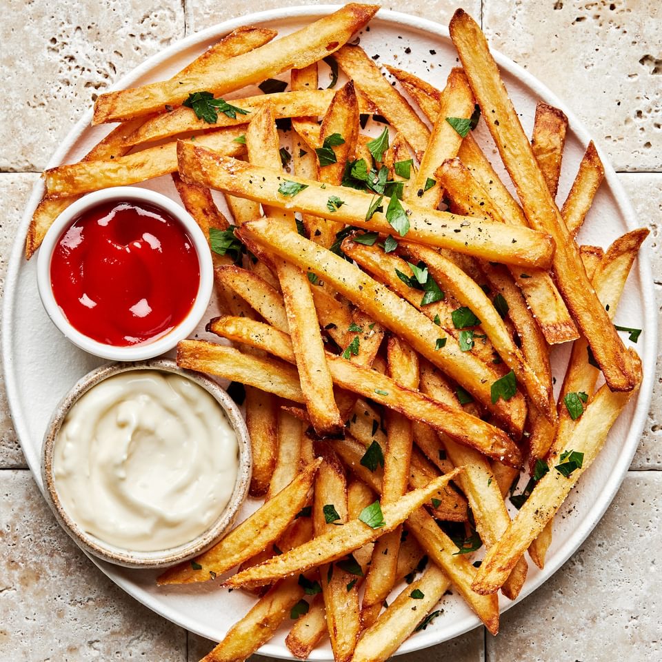 homemade French fries seasoned with salt and pepper, garnished with parsley and served with ketchup and garlic aioli