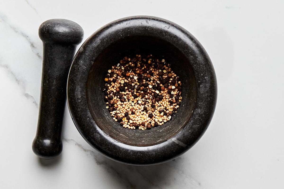 mustard seeds and peppercorns being crushed in a mortar and pestle