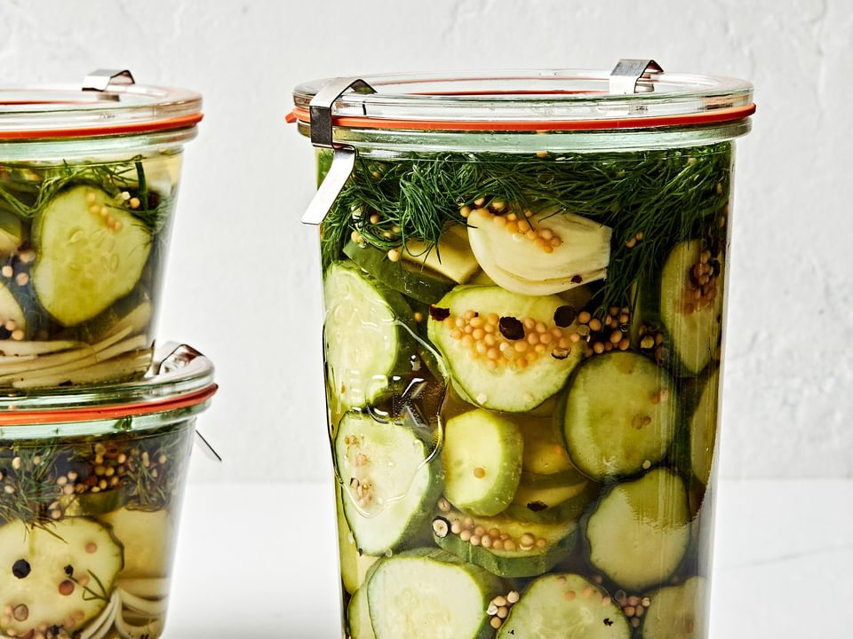 a large jar of homemade dill pickles next to two small jars of homemade pickles stacked on top of each other on the counter
