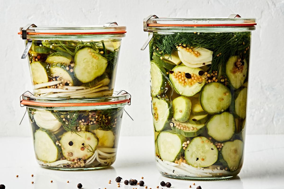 a large jar of homemade dill pickles next to two small jars of homemade pickles stacked on top of each other on the counter