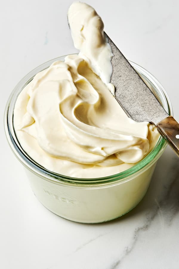 homemade mayonnaise in glass jar being scooped with a knife