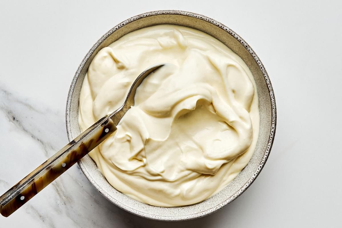 a bowl full of homemade mayonnaise being scooped with a spoon