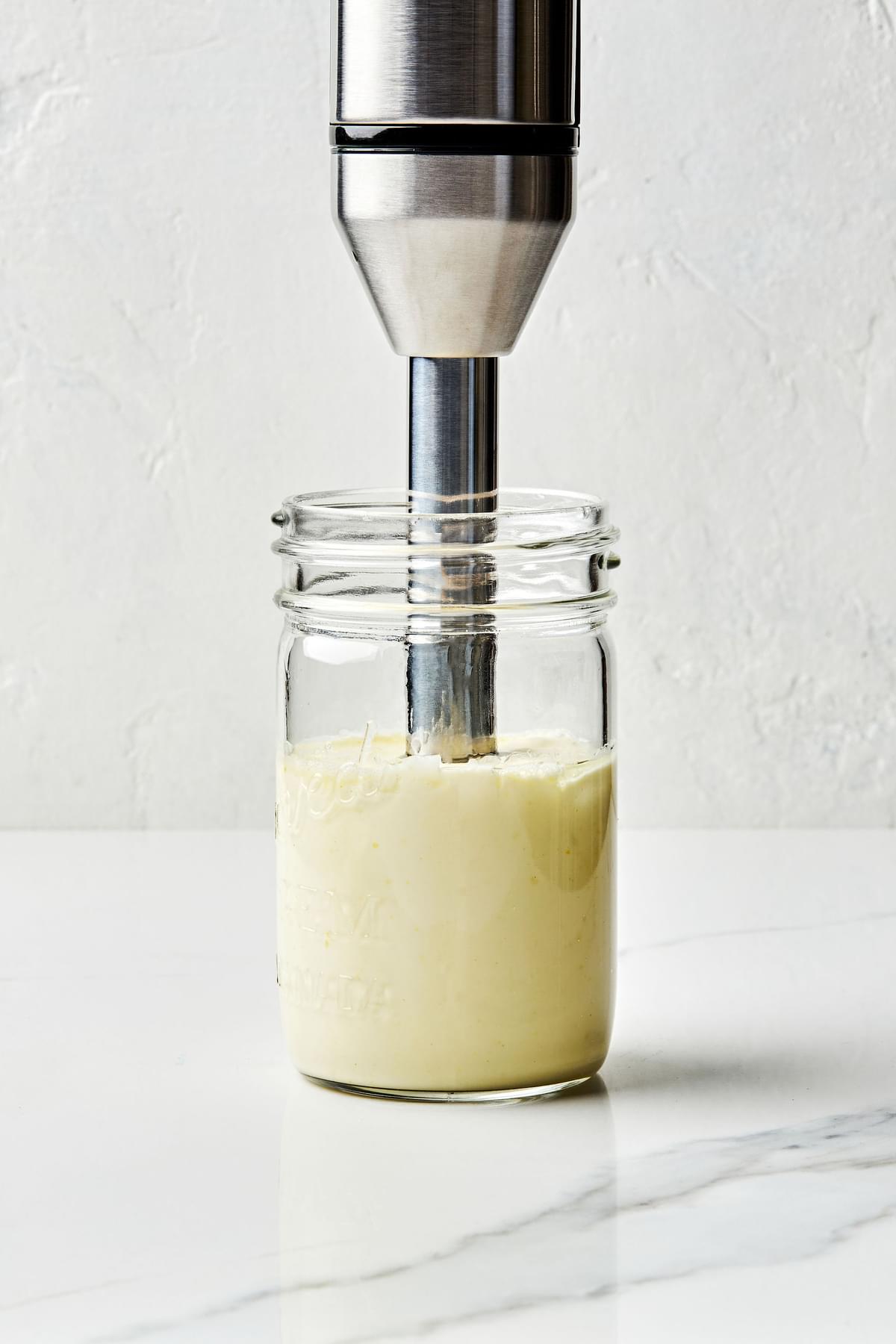 homemade mayonnaise being blended with an immersion blender in a glass mason jar