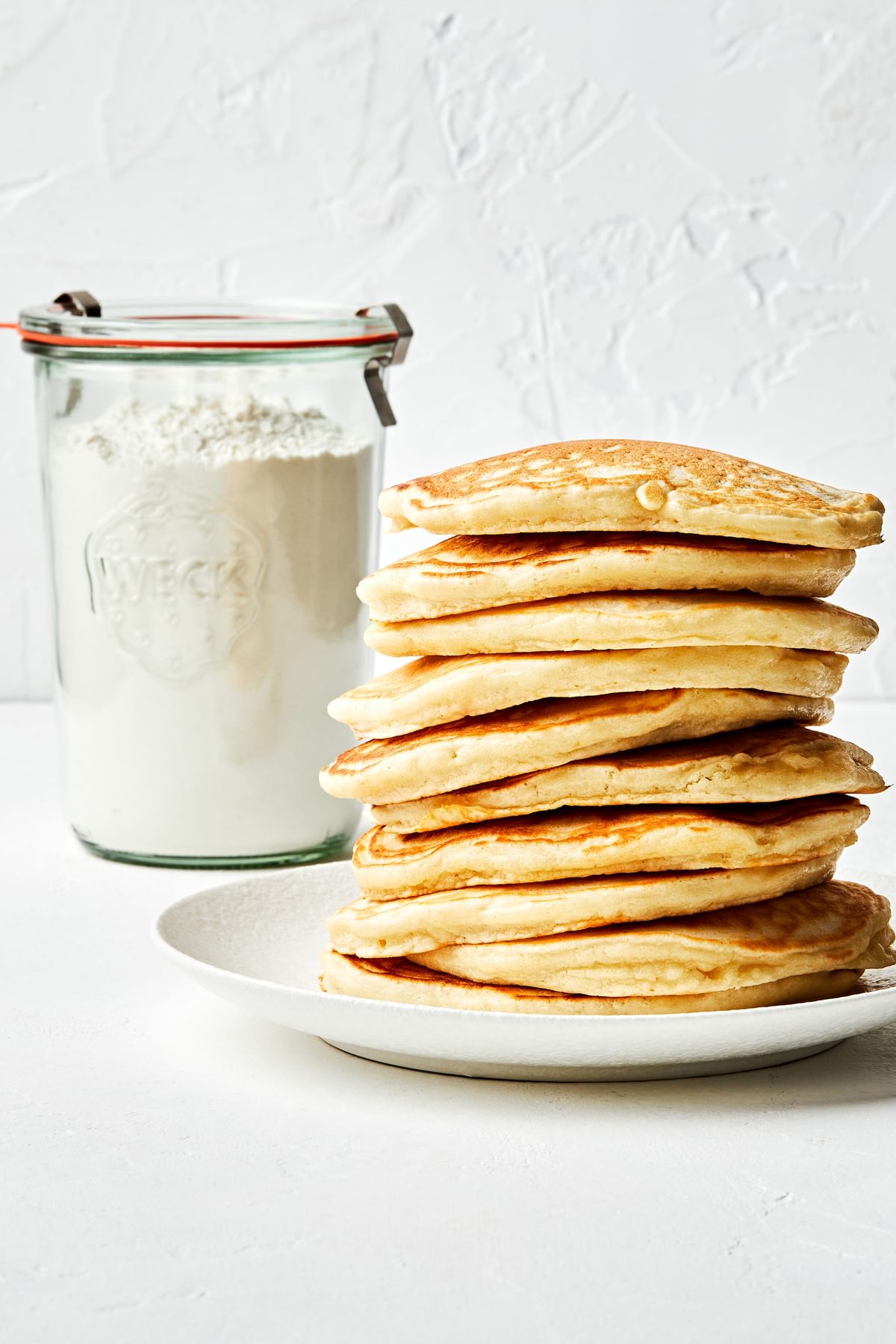 a stack of pancakes next to a jar of homemade pancake mix made with flour, sugar, baking powder, baking soda and salt