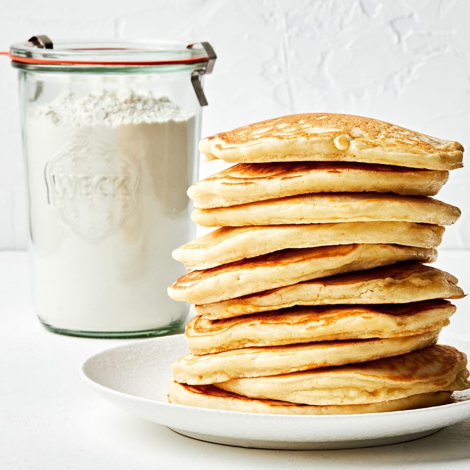 a stack of pancakes next to a jar of homemade pancake mix made with flour, sugar, baking powder, baking soda and salt