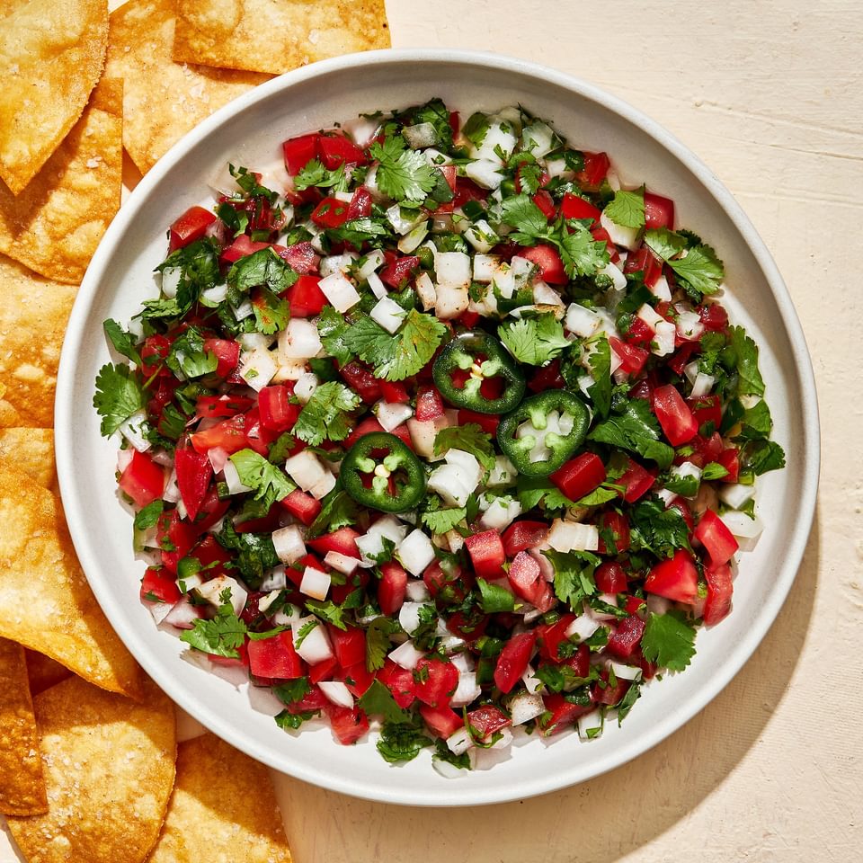 homemade pico de Gallo in a serving bowl surrounded by tortilla chips for serving