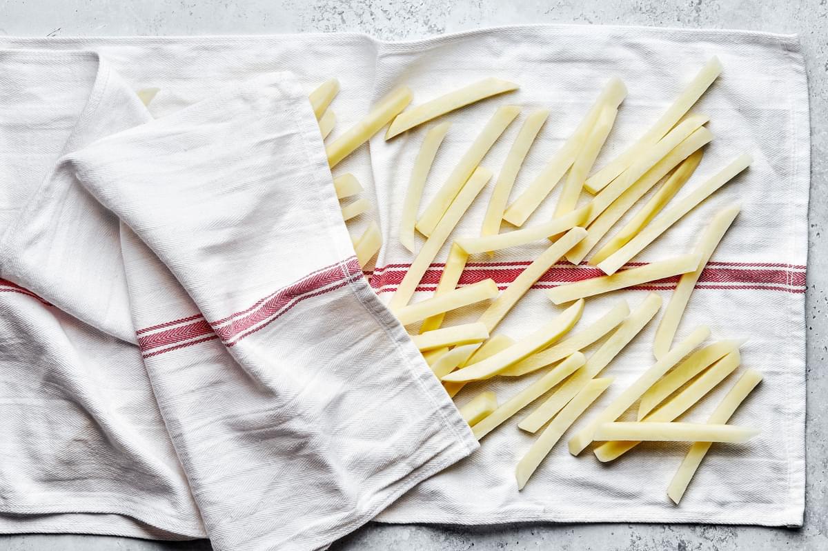 russet potatoes cut into fries being dried on a towel after soaking in a bowl of cold water