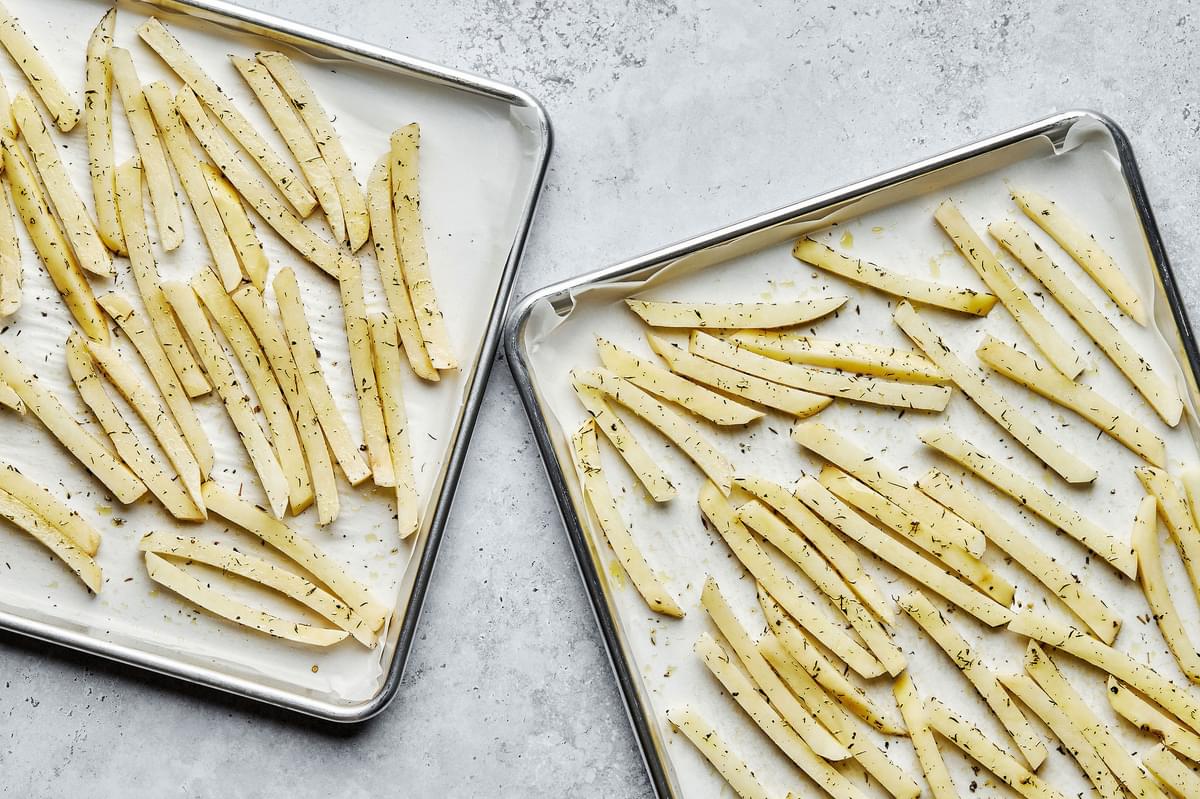 homemade fries tossed with olive oil, salt, pepper and thyme on a parchment lined baking sheet ready to go in the oven