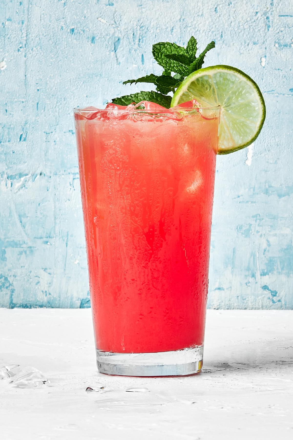 a glass of watermelon aqua fresca served over ice and garnished with fresh mint springs and a lime wedge