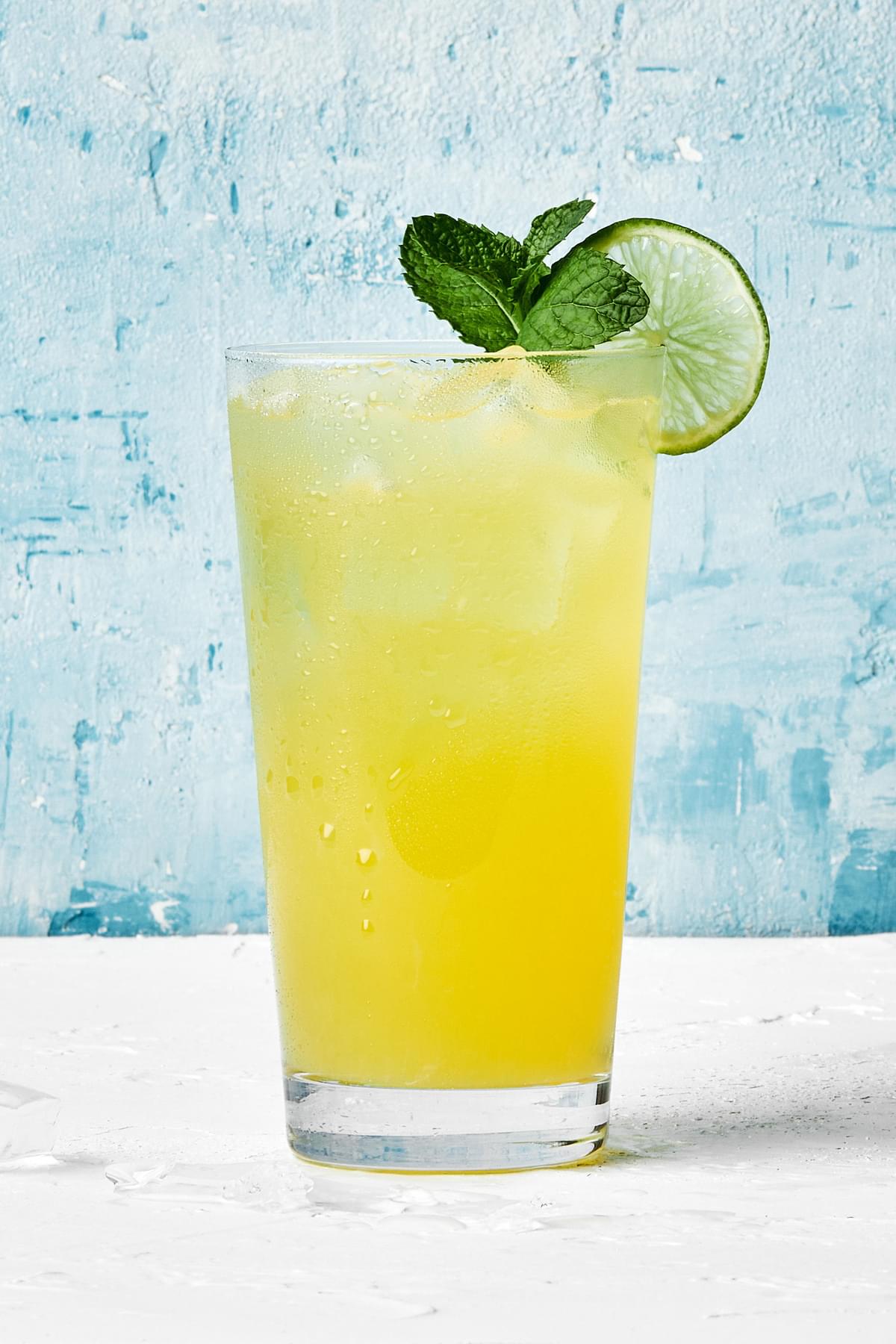 a glass of pineapple aqua fresca served over ice and garnished with fresh mint springs and a lime wedge