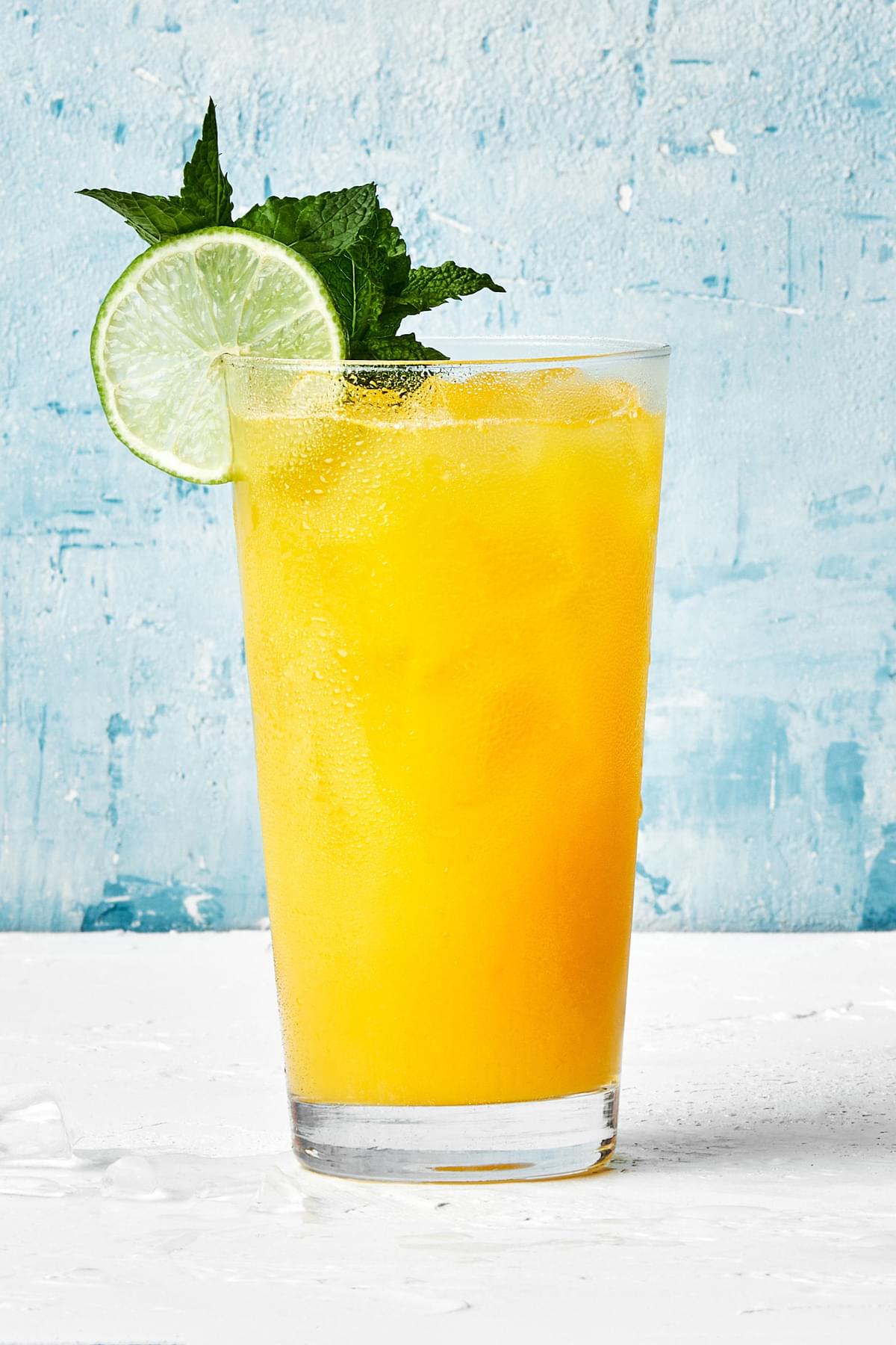 a glass of mango aqua fresca served over ice and garnished with fresh mint springs and a lime wedge