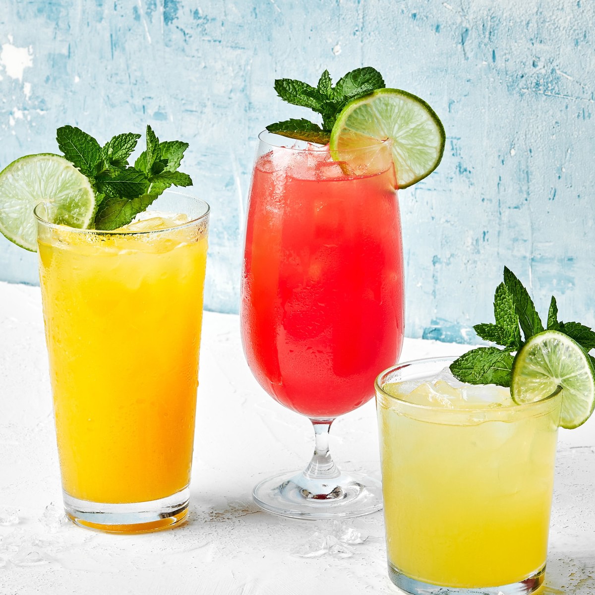 3 glasses of watermelon, mango and pineapple agua frescas garnished with fresh mint sprigs and lime wedges