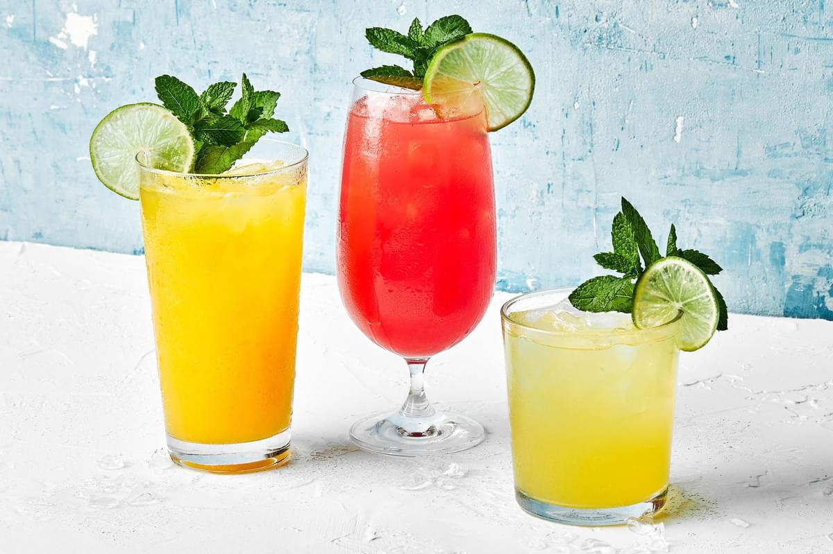 3 glasses of watermelon, mango and pineapple agua frescas garnished with fresh mint sprigs and lime wedges