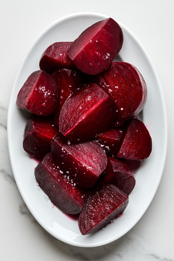homemade roasted beets cut into quarters on a serving platter, drizzled with olive oil and sprinkled with salt and pepper