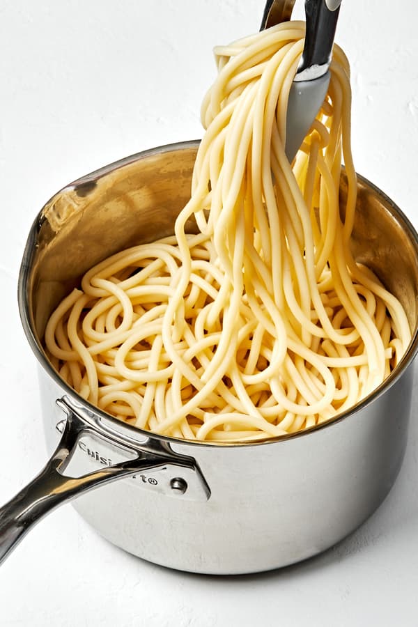 pasta noodles that have been cooked in salted water being pulled out of a pot with tongs