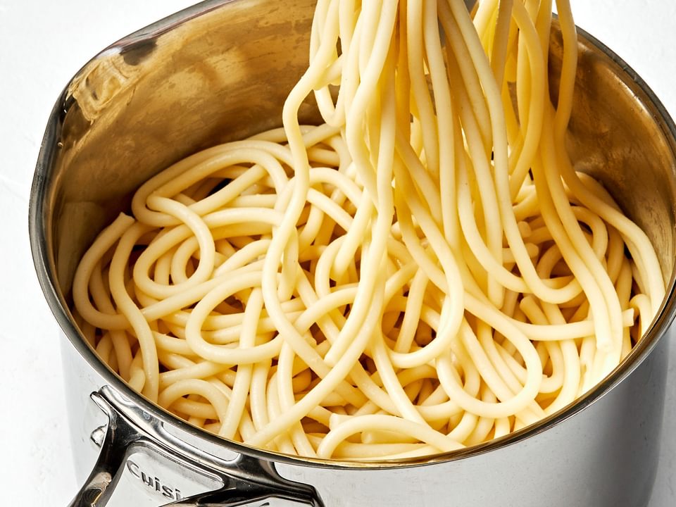 pasta noodles that have been cooked in salted water being pulled out of a pot with tongs