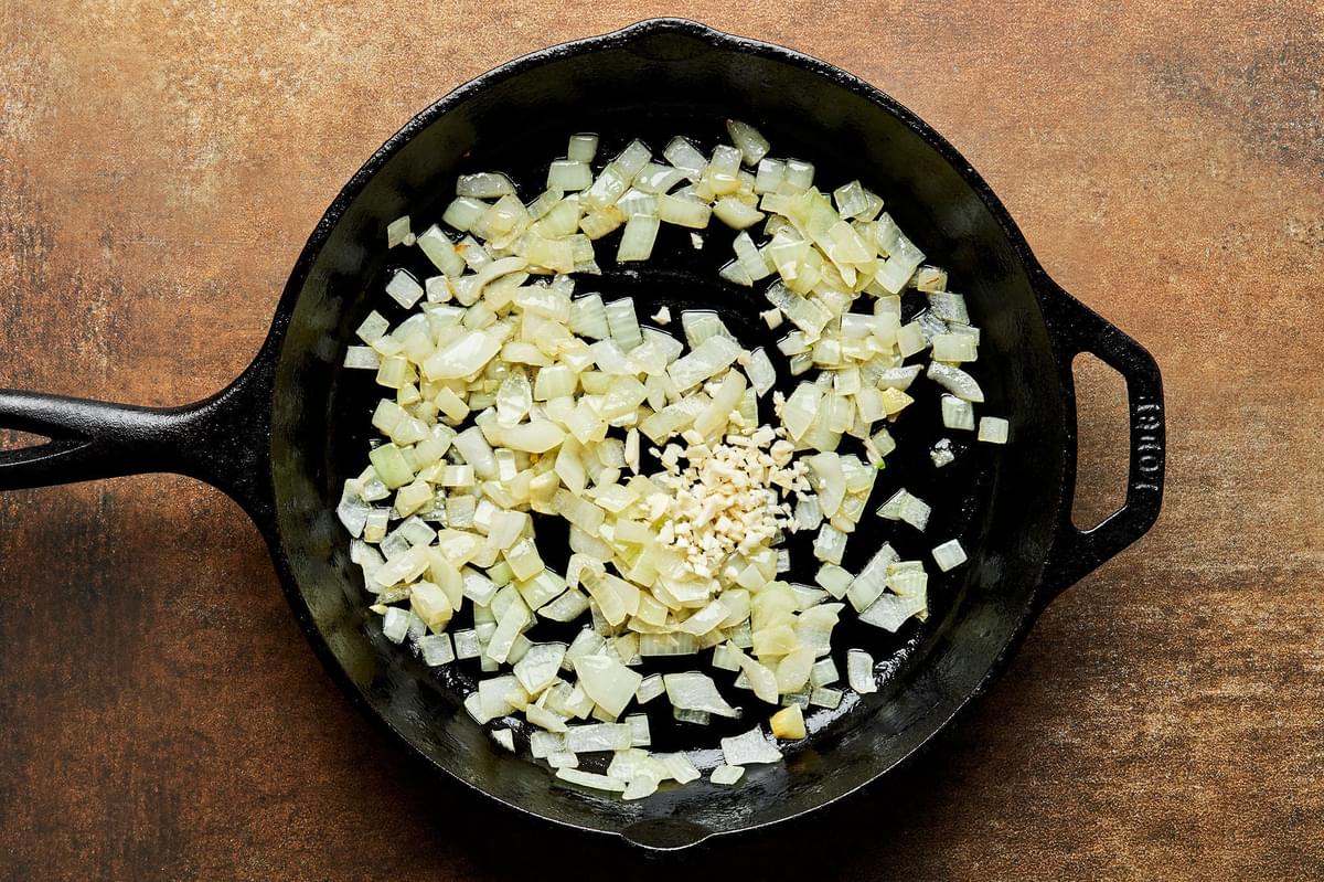 chopped onion being cooked in olive oil in a cast iron skillet for a homemade frittata