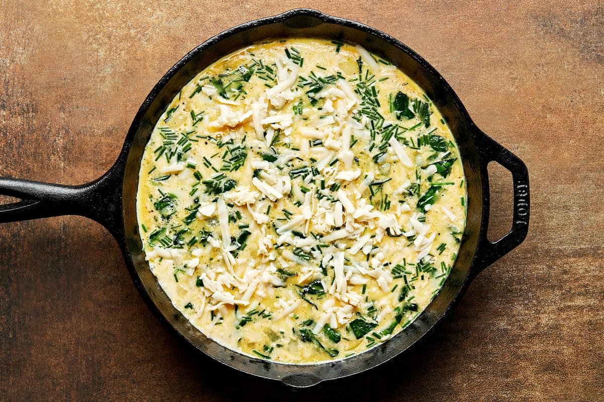 homemade frittata in a cast iron skillet ready to be baked in the oven, made with eggs, cream, veggies, cheese and seasonings