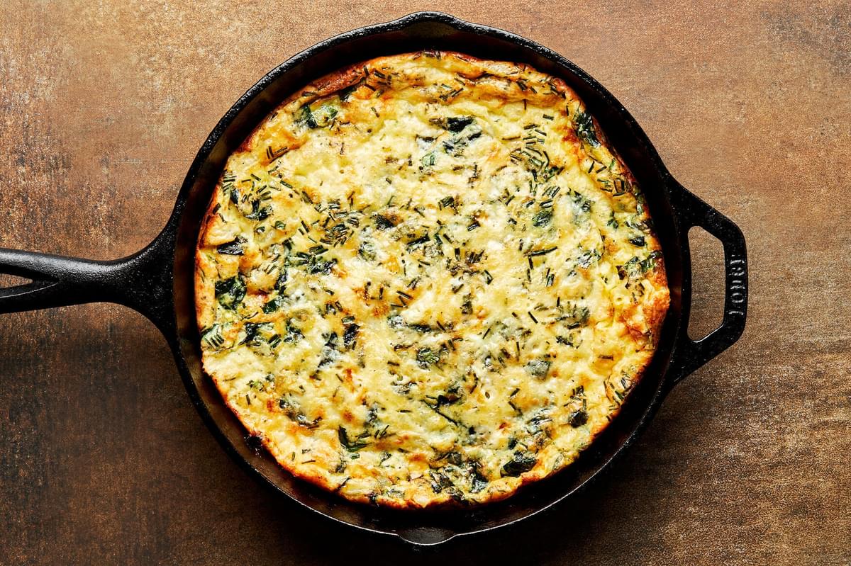 a homemade frittata in a cast iron skillet made with milk, eggs, cheese, herbs, spices and cheese